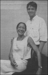 Barthelemy Fougea stands posed smiling behind a seated grinning Jenny Lee